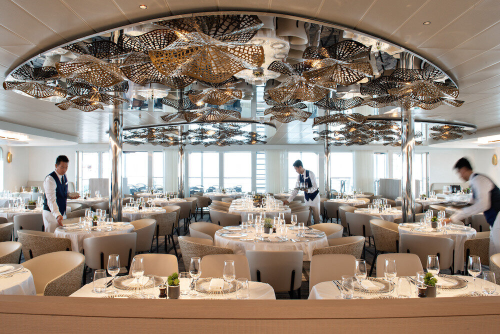 Hauptrestaurant der Le Bellot mit kunstvollem Deckenornament, weißen Tischdecken und Panoramafenstern