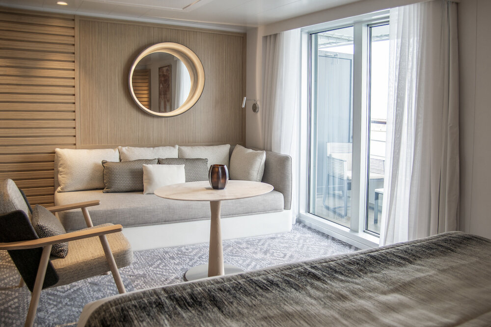 Elegante Sitzecke einer Privilege-Suite mit Sofa, rundem Spiegel und Balkonzugang auf einem Hochseekreuzfahrtschiff