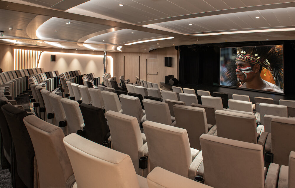 Modernes Bordkino der Le Bellot mit hellen Polstersesseln und Leinwand mit indigenem Motiv