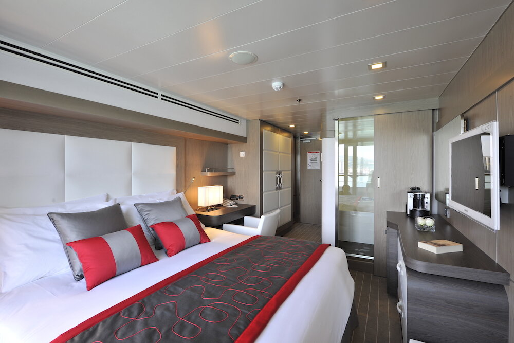 Deluxe-Balkonkabine der Le Boréal mit Doppelbett, roten Akzenten und Balkonzugang