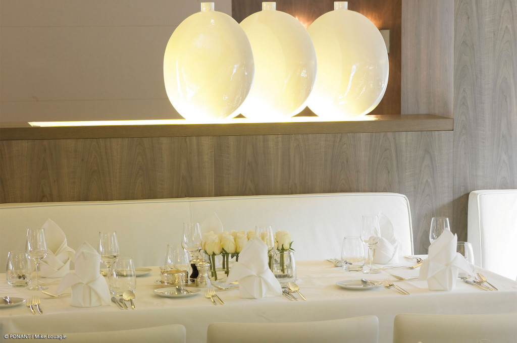 Festlich eingedeckter Tisch mit weißen Rosen und Weingläsern unter drei großen Kugelleuchten im Restaurant.