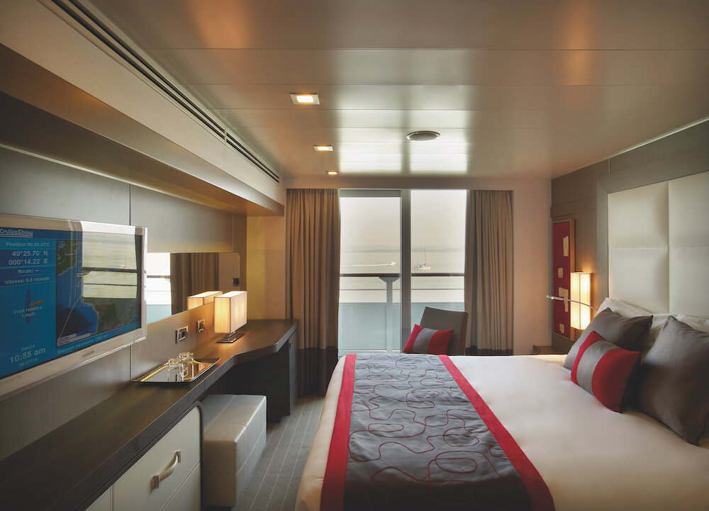 Moderne Prestige-Kabine der Le Boréal mit Doppelbett, roten Akzenten und Blick auf den Balkon.