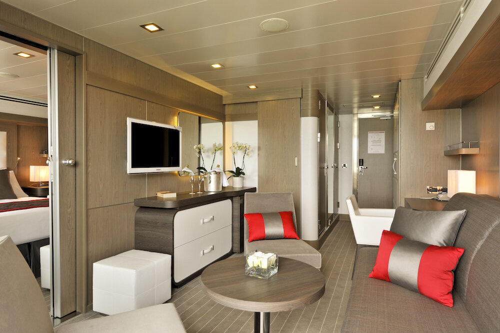 Wohnbereich der Prestige Suite der Le Boréal mit Sofa, roten Akzenten und offener Verbindung zum Schlafzimmer.