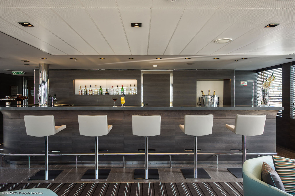 Bar mit langem Tresen und fünf weißen Barhockern an Bord der Le Soléal.