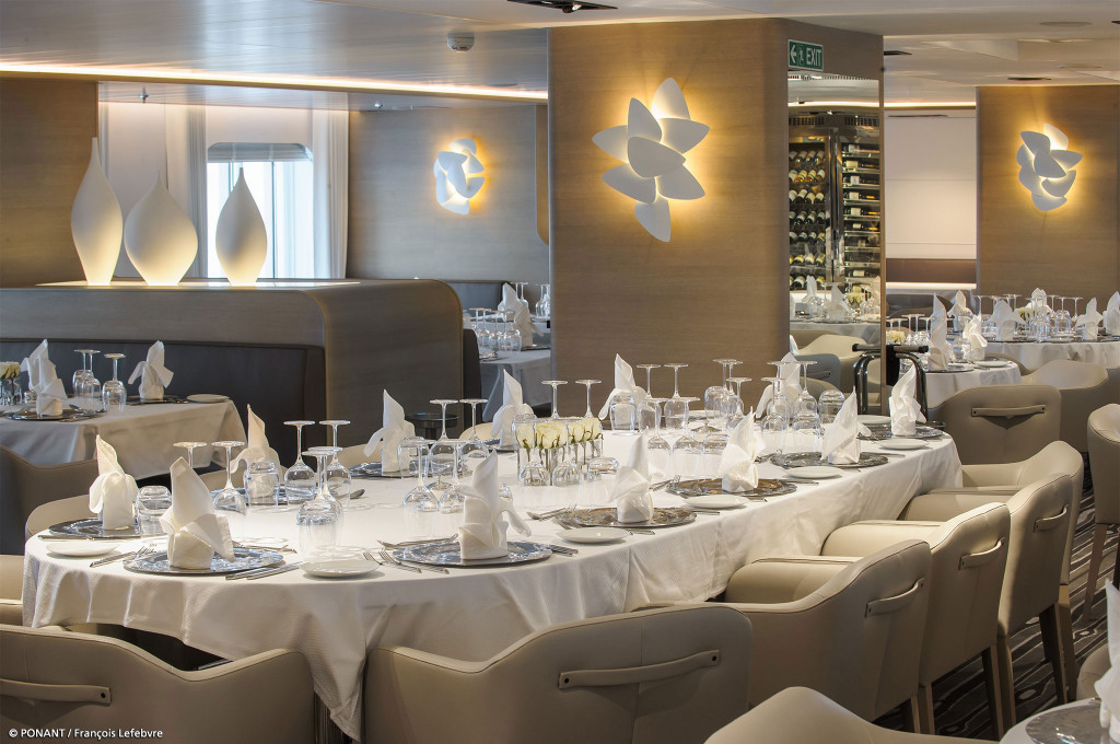 Eingedeckter Restauranttisch mit Servietten und Weingläsern neben beleuchteten Wandobjekten an Bord der Le Soléal.