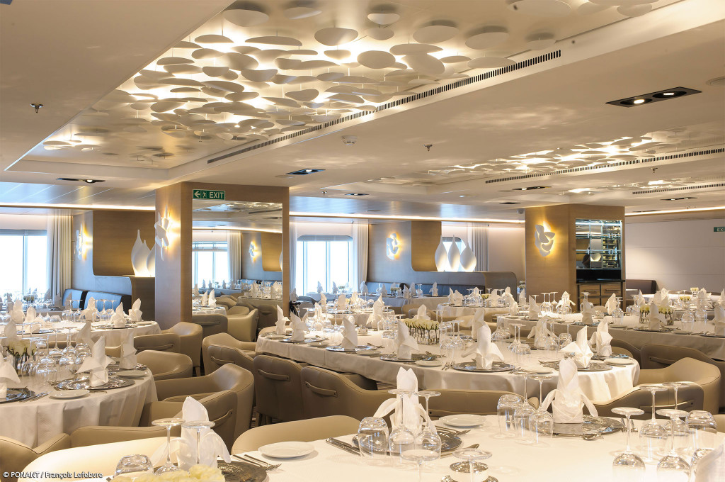 Eingedeckter Speisesaal mit weißen Tischen, gefalteten Servietten und skulpturaler Deckenbeleuchtung an Bord der Le Soléal.