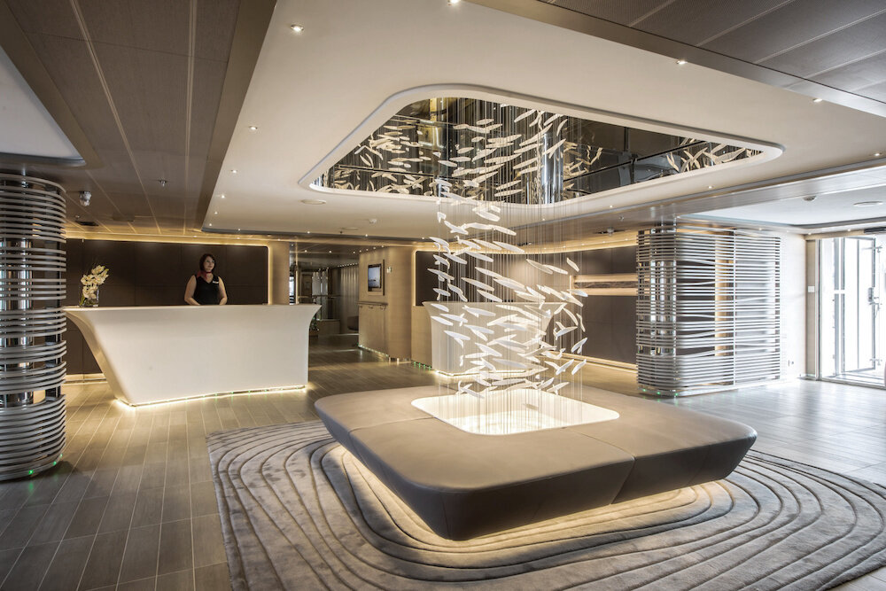 Modernes Atrium mit weißem Empfangstresen, hängender Fischschwarm-Lichtinstallation und silbernen Metallsäulen