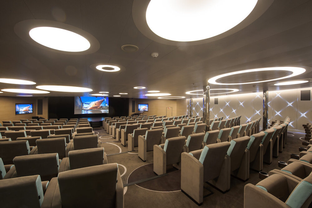 Moderner Kino- und Vortragssaal mit Reihenbestuhlung in Grau und Türkis, Leinwand und kreisförmigen Deckenlichtern