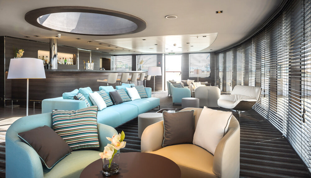 Moderne Lounge mit türkisfarbenen Sofas, Loungesessel, Panoramafenstern und Bar im Hintergrund