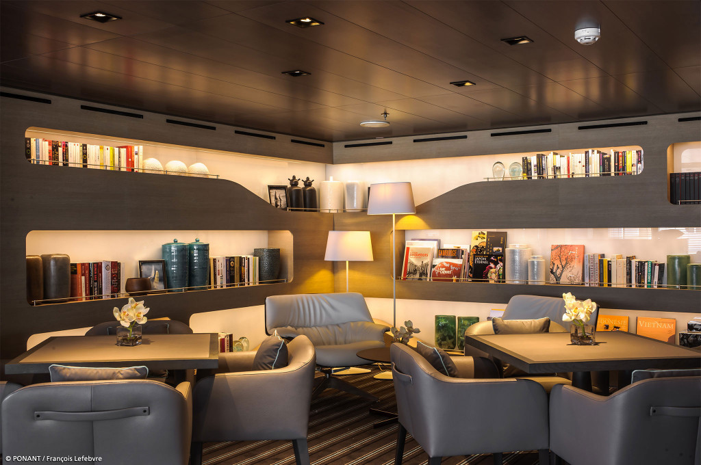 Bibliothek mit beleuchteten Bücherregalen und Sitzgruppe im Halbdunkel an Bord der Le Soléal.