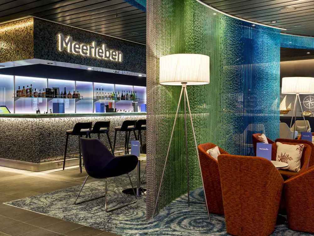 Bar Meerleben auf einem Kreuzfahrtschiff mit illuminierter Mosaikwand, Barhockern und orangefarbenen Loungessesseln