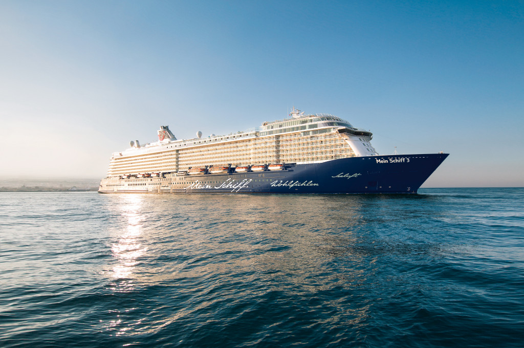 Mein Schiff 3 Kreuzfahrtschiff in voller Fahrt auf dem Meer mit sonnigem Wetter.