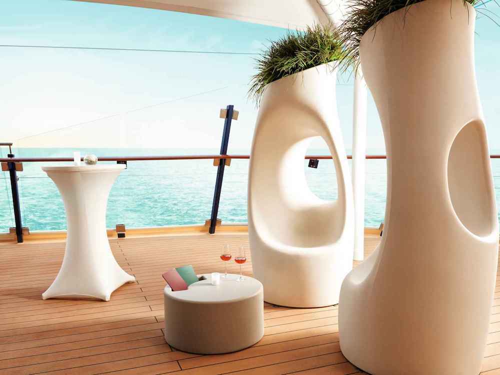 Moderner Außenbereich auf dem Deck von Mein Schiff 3 mit weißen Designskulpturen, Stehtisch und zwei Weingläsern vor dem Meer