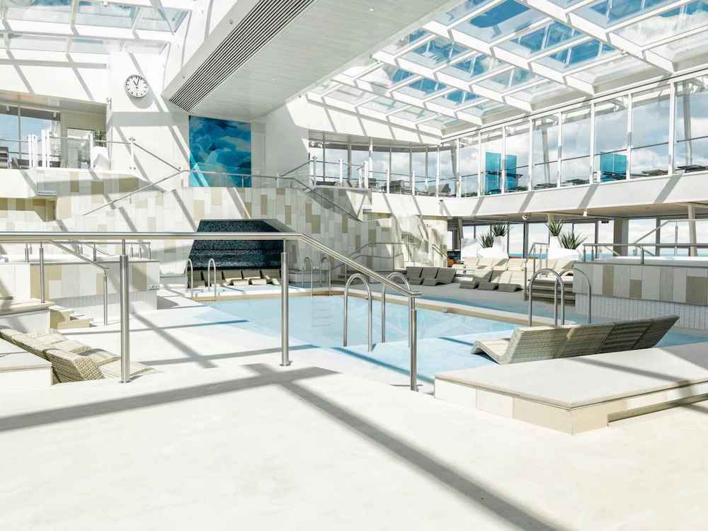 Helles Hallenbad mit Glasdach, Pool, Whirlpool und Liegestühlen auf mehreren Ebenen