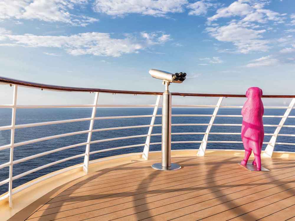 Ausguck auf dem Sonnendeck mit Fernrohr, pinker Hundeskulptur und Reling mit Meeresblick auf einem Kreuzfahrtschiff
