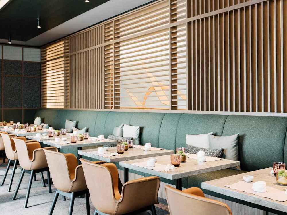 Modernes Restaurant mit langer grüner Bankettsitzbank, Holzlamellenverkleidung und Marmorplatten auf einem Luxuskreuzfahrtschiff