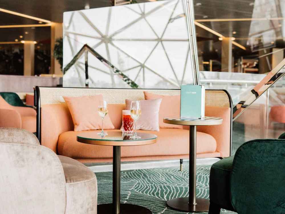 Diamant Bar der Mein Schiff 4 mit lachrosa Sofa, Cocktailgläsern und geometrischer Raumstruktur im Hintergrund