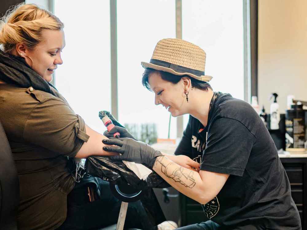 Tattookünstlerin tätowiert einem Gast den Arm im Tattoostudio eines Hochseekreuzfahrtschiffes