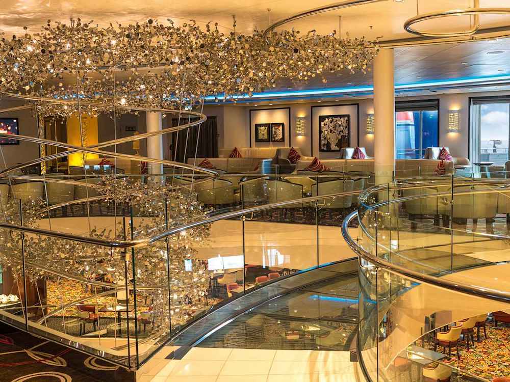 Prachvolles Atrium mit spektakulärem Kronleuchter, geschwungenem Glasgeländer und Lounge-Bereichen auf mehreren Ebenen auf einem Kreuzfahrtschiff
