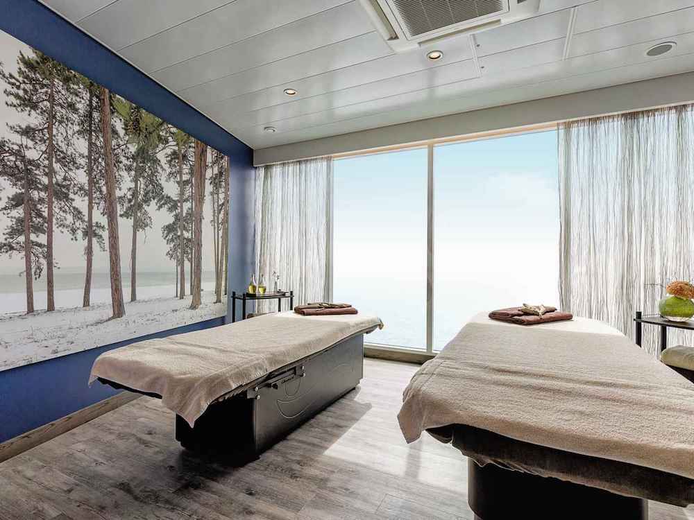 Spa-Behandlungsraum der Mein Schiff 4 mit zwei Massageliegen, Waldmotiv-Wandbild und Panoramafenster mit Meerblick
