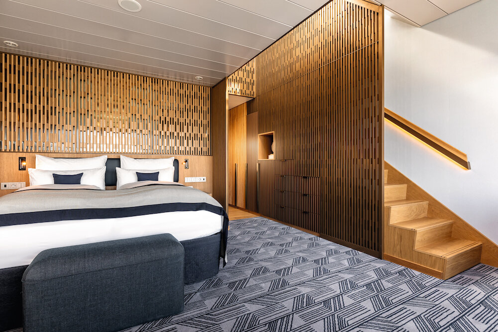Maisonette-Suite mit Doppelbett, vertikal gerillter Holzwand und Holztreppe zum Obergeschoss