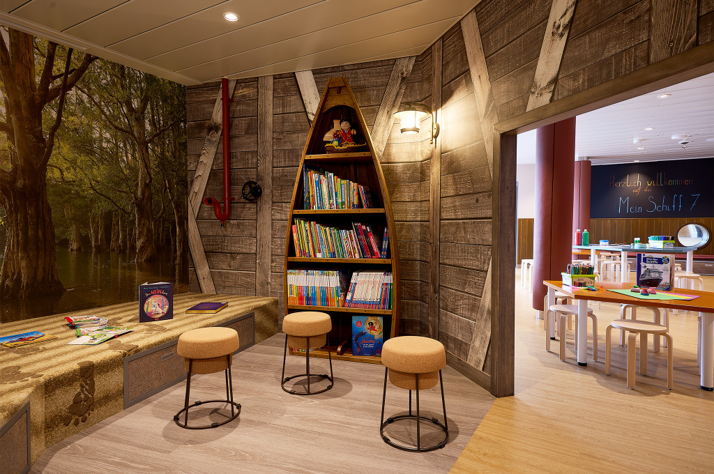 Leseecke im Kids-Club mit bootsförmigem Bücherregal, Hockern und Bastelbereich für Kinder.