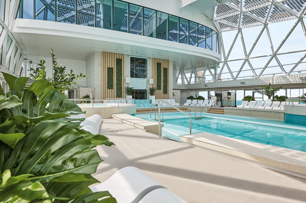 Innenpool mit angrenzendem Whirlpool, weißen Liegestühlen und lichtdurchfluteter Glaskuppel.