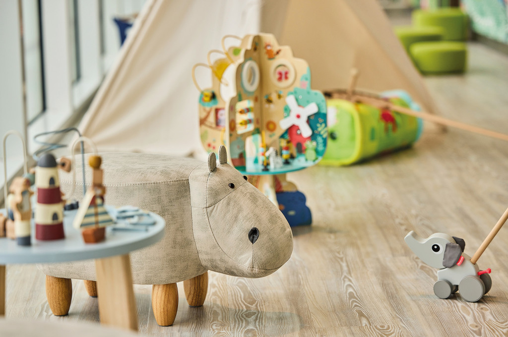Detailaufnahme im Babyraum Nest mit Nilpferd-Hocker, Holzspielzeug und Motorikspielen.