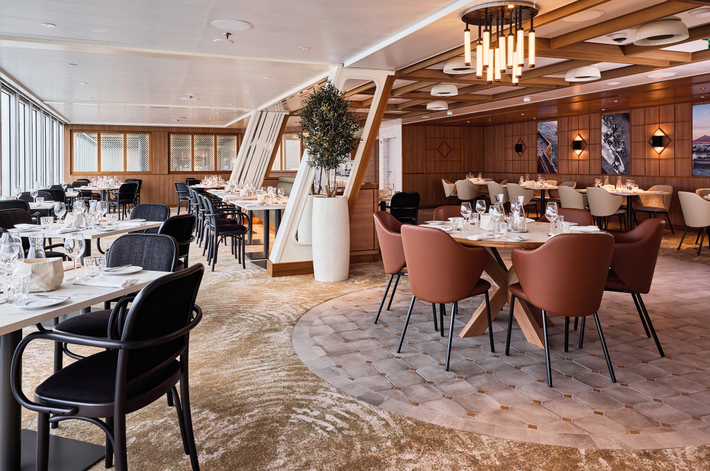Osteria Restaurant mit rundem Esstisch, braunen Lederstühlen und zentralem Olivenbaum als Dekoration.