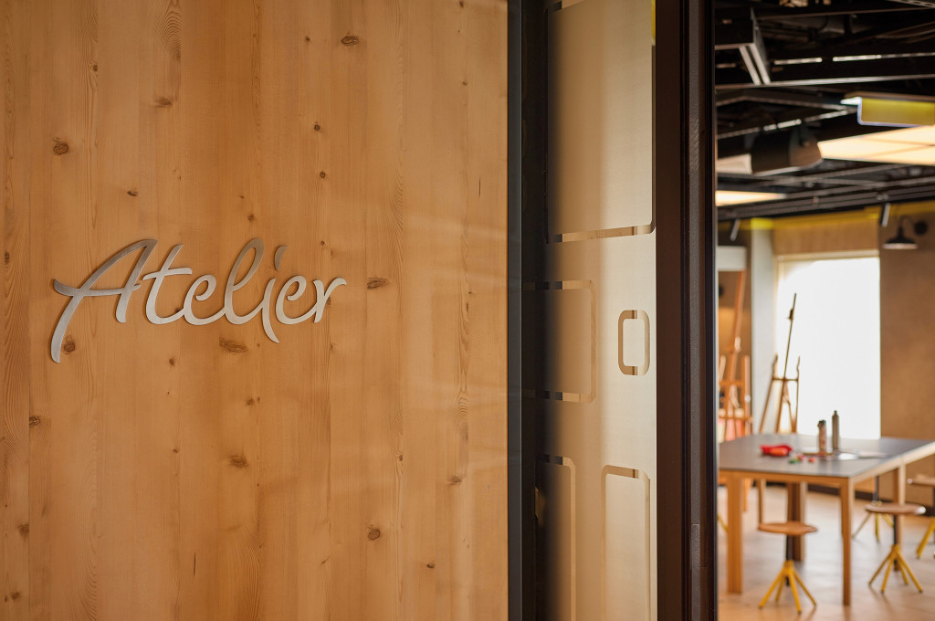 Eingang zum Atelier mit dem Schriftzug auf einer Holzwand und Blick auf den Kreativbereich.