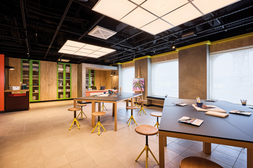 Kreativ-Atelier mit Arbeitstischen, Hockern, Staffelei und Materialschränken für Malworkshops.