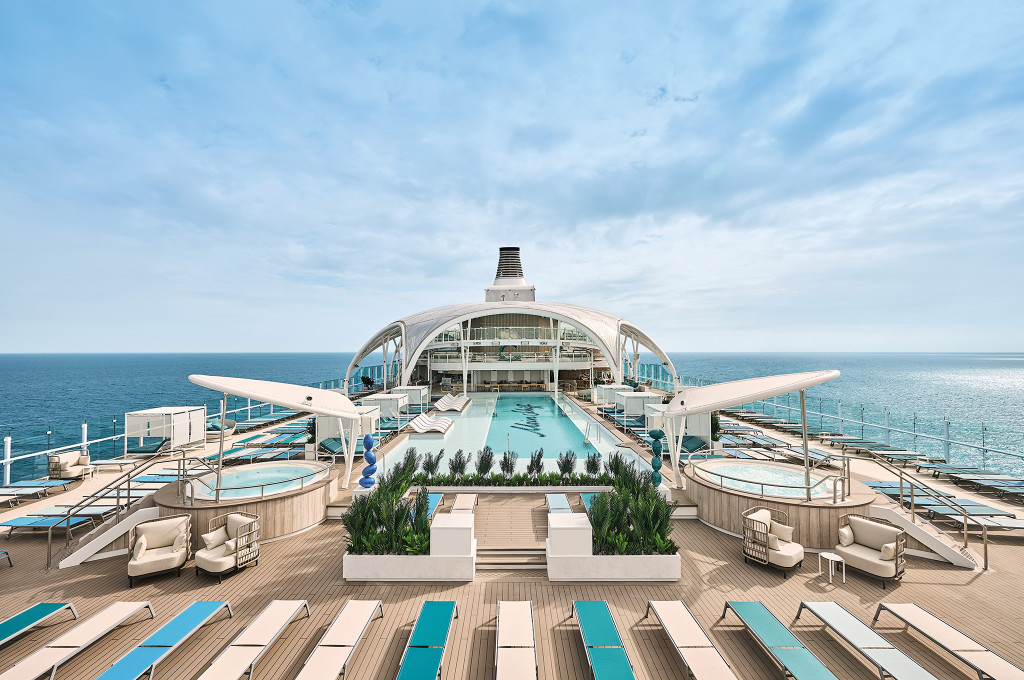 Symmetrische Ansicht des Pooldecks mit zentralem Außenpool, seitlichen Whirlpools und Liegestuhlreihen unter markantem Bogendach mit Meerblick.