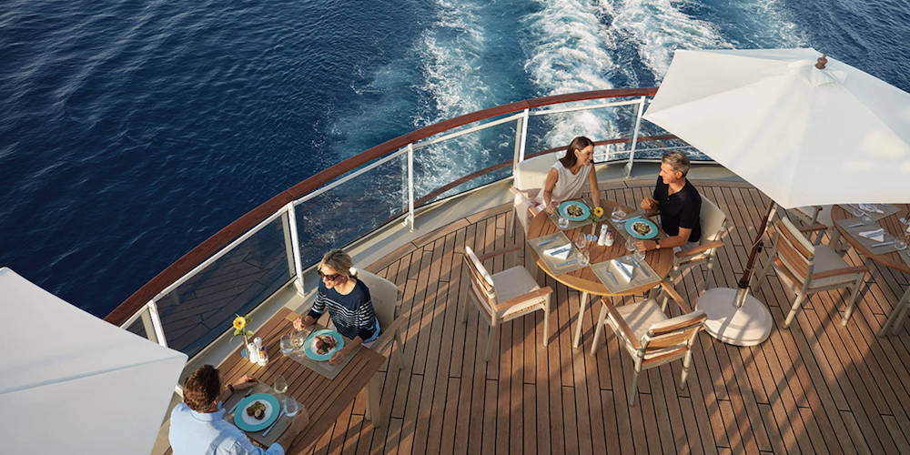 Gäste beim Mittagessen auf dem Achterdeck-Restaurant der MS Europa 2 mit Teakholzdeck und Blick auf das Kielwasser