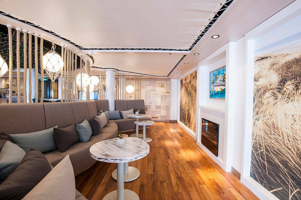 Lounge mit maritimem Seildekor, geflochtenen Kugelleuchten, grauem Sofa und Marmortischen auf einem Kreuzfahrtschiff