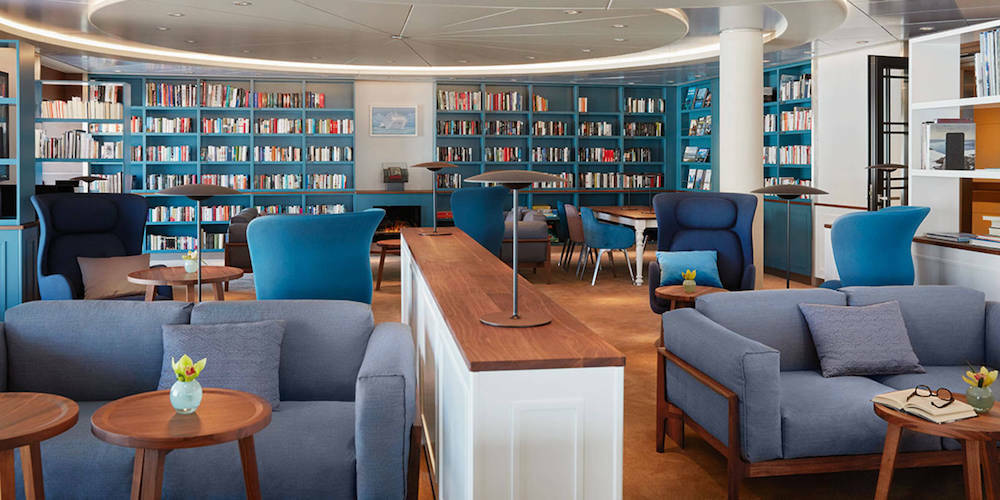 Eleganter Bibliotheks-Loungebereich der MS Europa 2 mit blauen Bücherregalen, Sesseln und Sofas.
