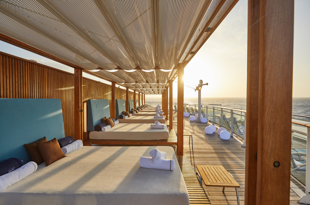 Reihe von Cabana-Liegebetten auf dem Sonnendeck mit Teakholzrahmen im warmen Abendlicht eines Sonnenuntergangs am Meer