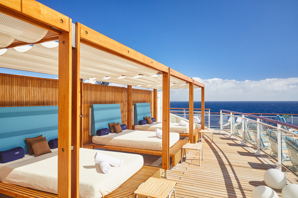 Sonnendeck mit privaten Cabana-Liegebetten aus Teakholz, cremefarbenen Sonnensegeln und blauem Meerblick