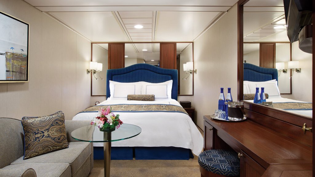 Elegante Innenkabine mit marineblauem Polsterkopfteil, Doppelbett, Sofa und Schminktisch mit Blumen