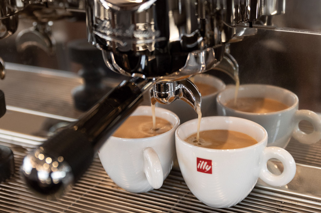 Frisch gebrühter Espresso läuft aus einer Siebträgermaschine in weiße Tassen im Bordcafé eines Hochseekreuzfahrtschiffes.
