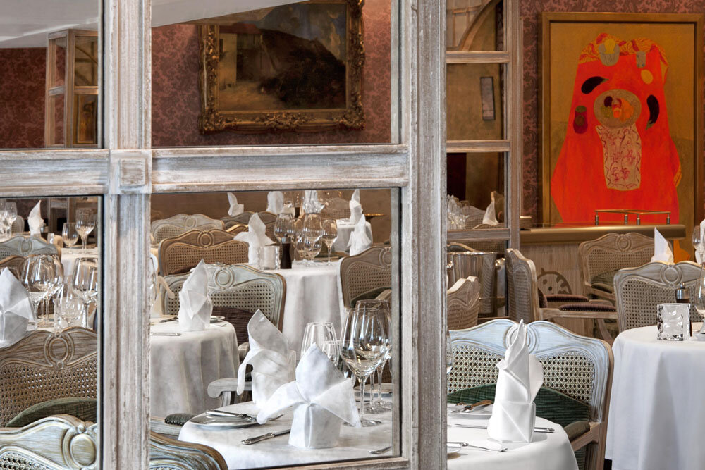 Klassisches Restaurant im französischen Stil mit Korbstühlen, weißen Tischdecken und Ölgemälden an der Wand