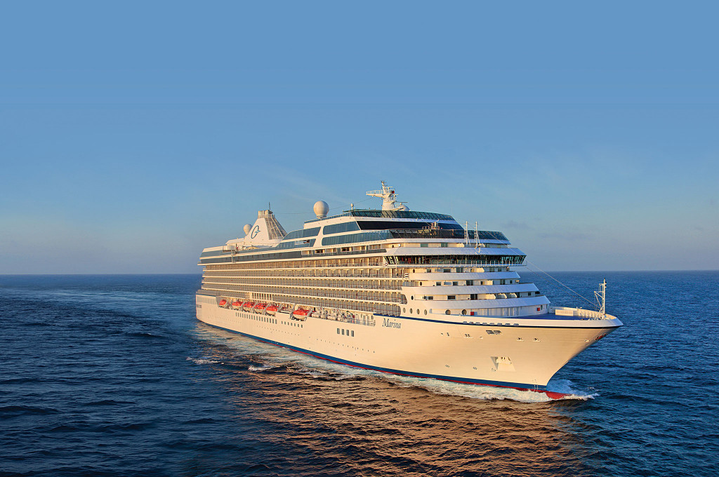 Hochseekreuzfahrtschiff fährt bei klarem Himmel auf offener See, mehrere Decks und Rettungsboote sichtbar.