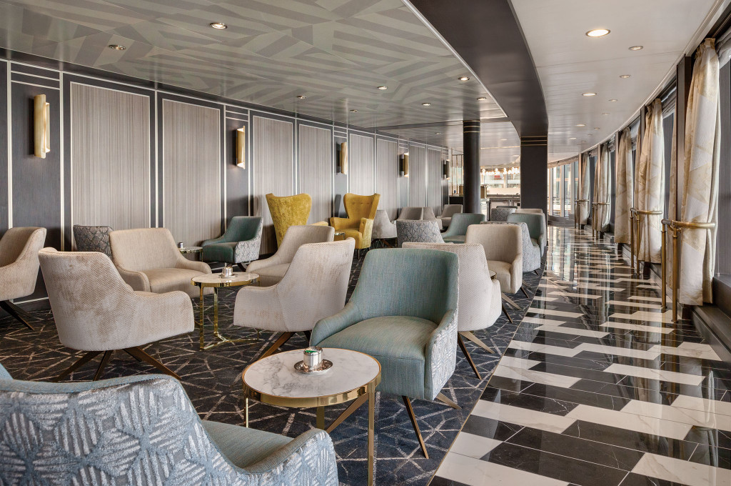Elegante Bordlounge mit gepolsterten Sesseln, Marmorboden und Wandleuchten an Bord eines Hochseekreuzfahrtschiffes.