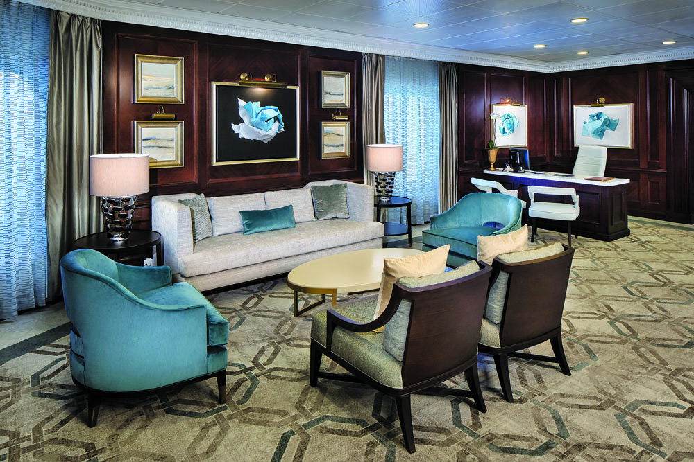 Elegantes Suiten-Wohnzimmer mit türkisfarbenen Samtsesseln, weißem Sofa, dunkler Mahagonivertäfelung und Kunstgemälden