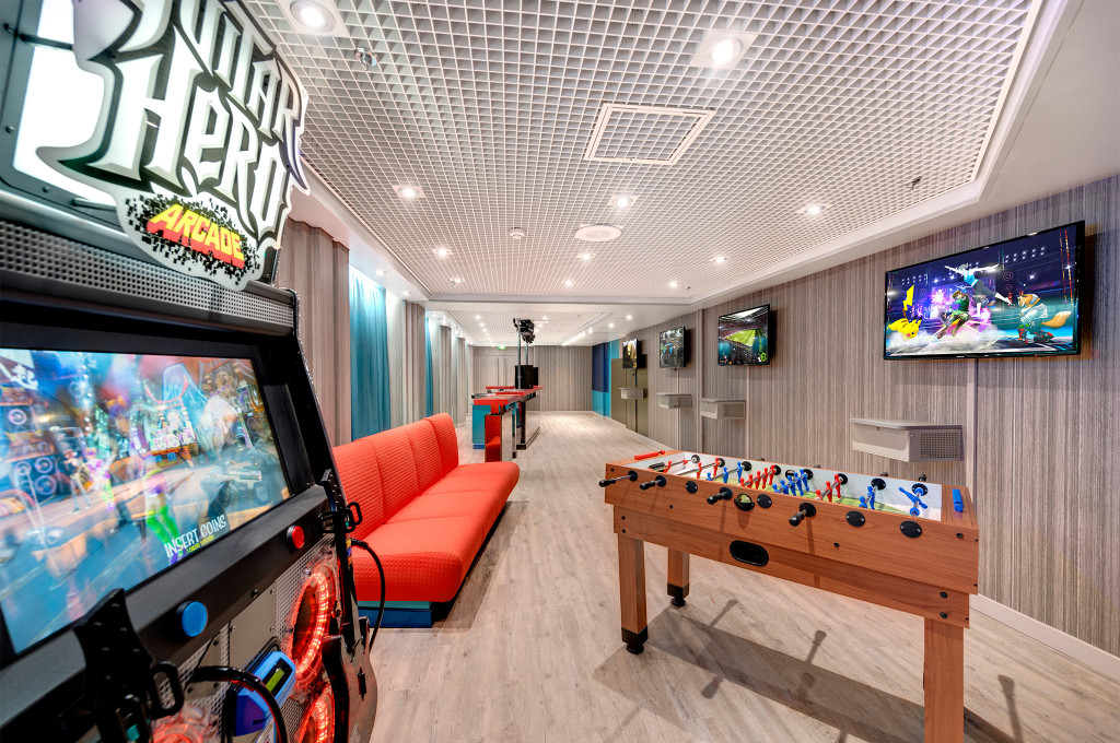 Spielhalle mit Guitar-Hero-Arcade-Automat, Tischkicker, roter Sitzbank und Flachbildschirmen an Bord