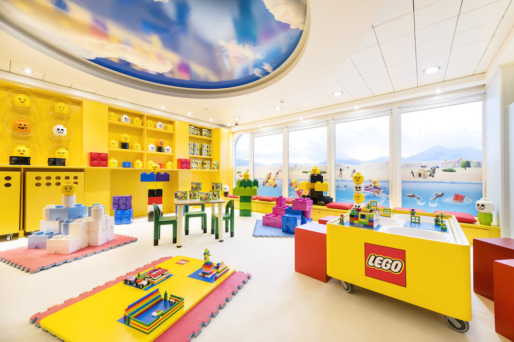 Heller LEGO-Kinderspielbereich mit großen Steinen, Basteltischen und Panoramafenstern auf einem Hochseekreuzfahrtschiff