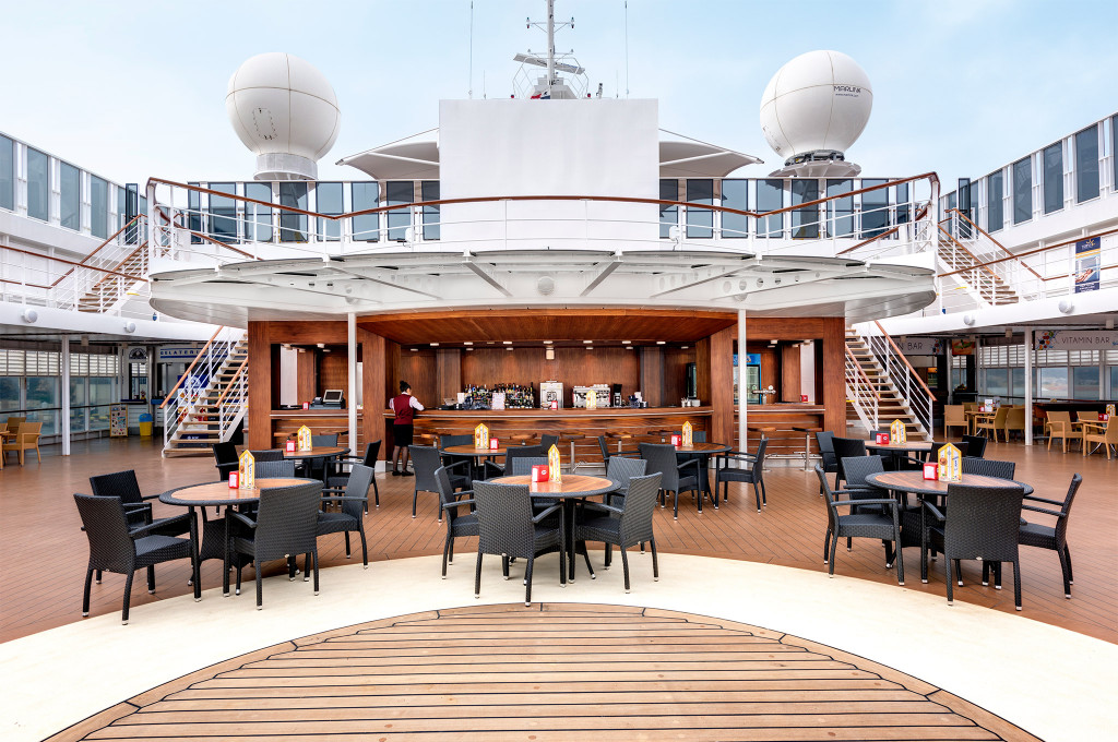 Außenbar auf dem Pooldeck mit runden Tischen, Rattanstühlen und zentraler Bartheke auf einem Kreuzfahrtschiff