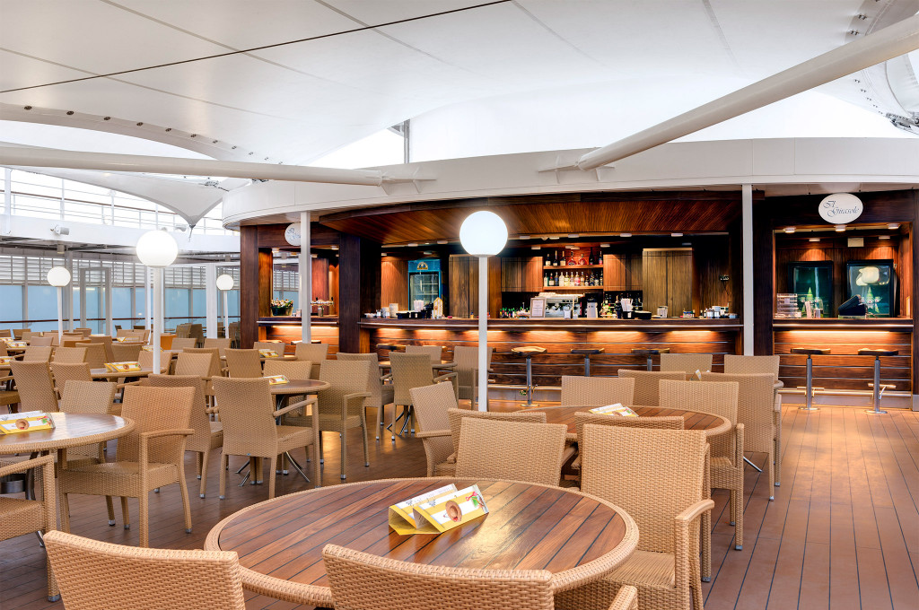 Halboffenes Restaurant mit Rattan-Stühlen, Holztischen und Bartheke auf dem Sonnendeck eines Kreuzfahrtschiffes