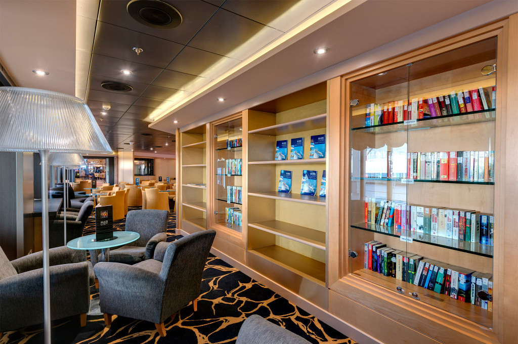 Bibliothekslounge mit großen Bücherregalen, Sesseln und angrenzendem Loungebereich auf einem Kreuzfahrtschiff