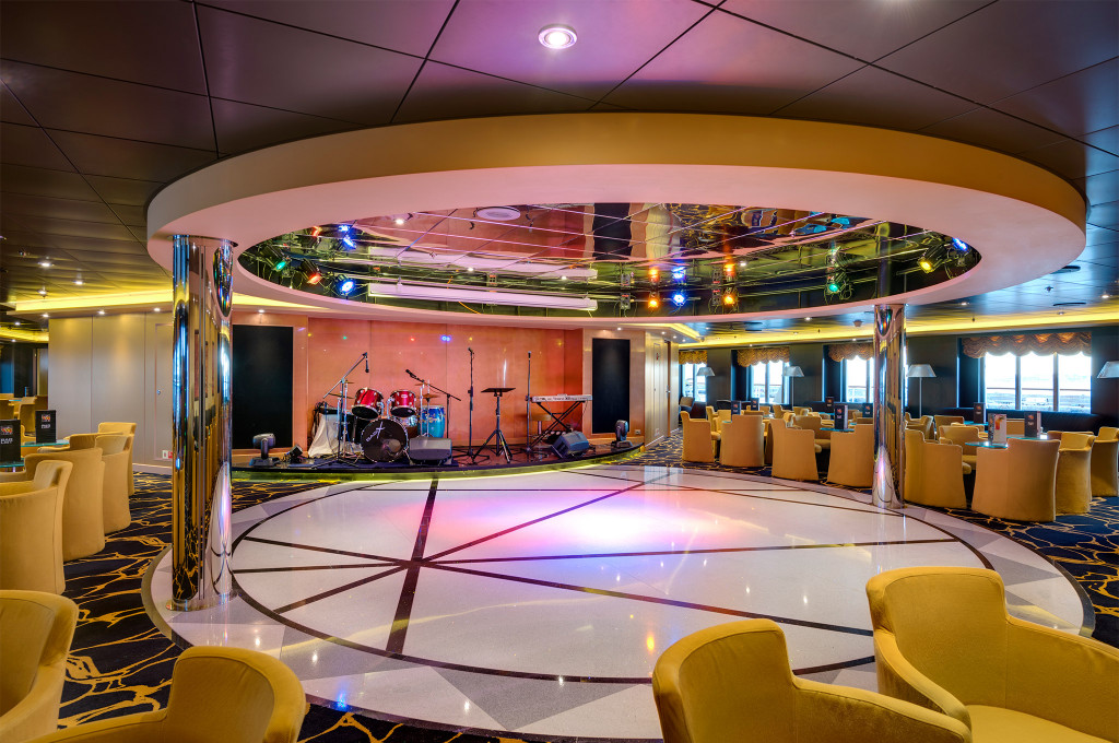 Showlounge mit rundem Tanzboden, Bühne mit Schlagzeug und goldgelben Sesseln auf einem Kreuzfahrtschiff