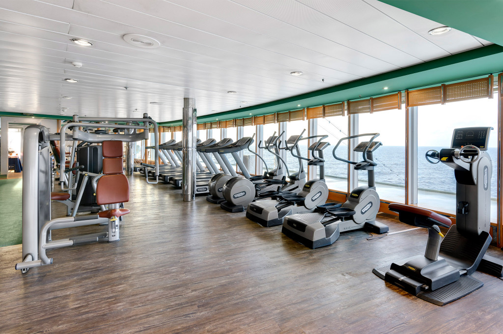 Fitnessstudio mit Laufbändern, Ellipsentrainern und Panoramafenstern zum Meer auf einem Kreuzfahrtschiff